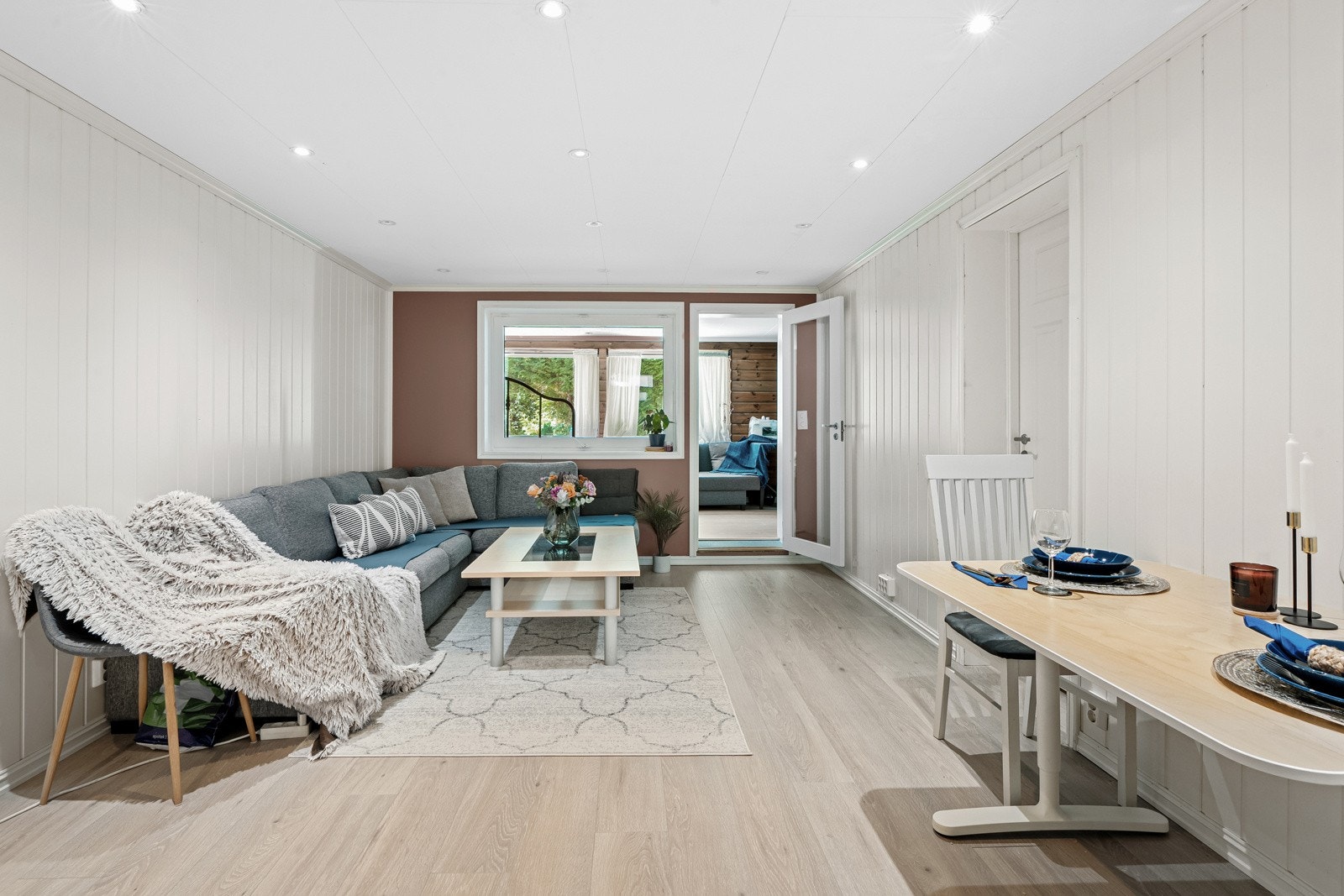 Stuen har samme laminatgulv, lysmalte panelvegger, to glatte, malte vegger og himling med downlights. Rommet har god plass til sofa, tv-løsning og et frokostbord. Galleribilde