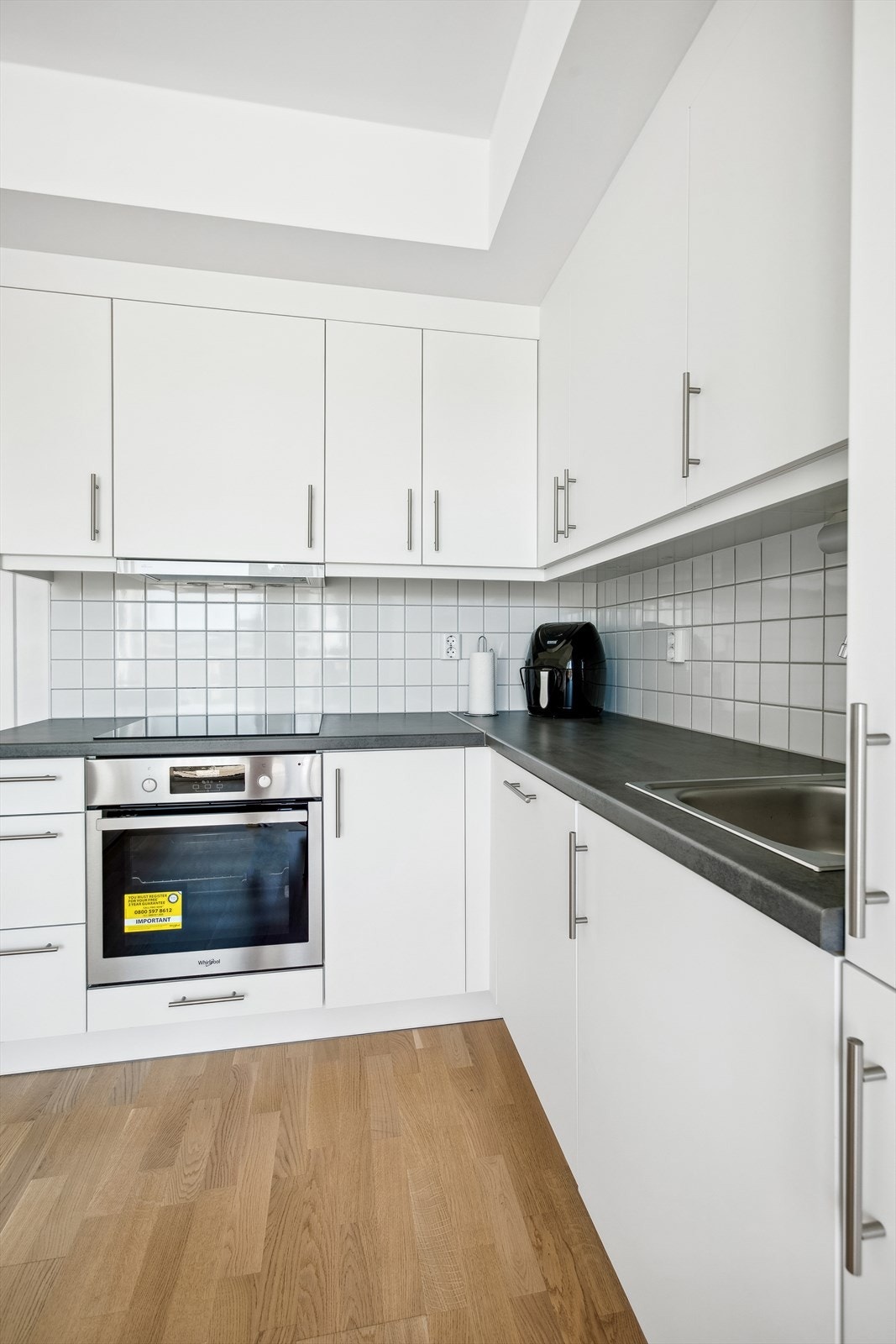 Kjøkkeninnredning med hvite glatte fronter og laminert benkeplate. Integrert komfyr med nedfelt induksjonstopp, oppvaskmaskin og mekanisk ventilator koblet til avtrekkskanal. Galleribilde