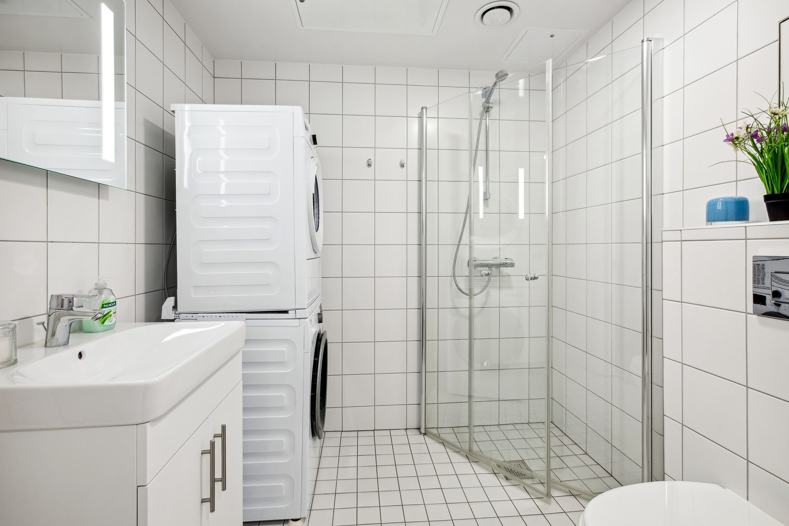 Badet består av flislagt gulv med elektrisk gulvvarme og flislagte vegger. Vegghengt servantskap med heldekkende servant og ett-greps armatur. Dusjnisje med innfellbare glassdører. Opplegg for vaskemaskin og tørketrommel. Galleribilde