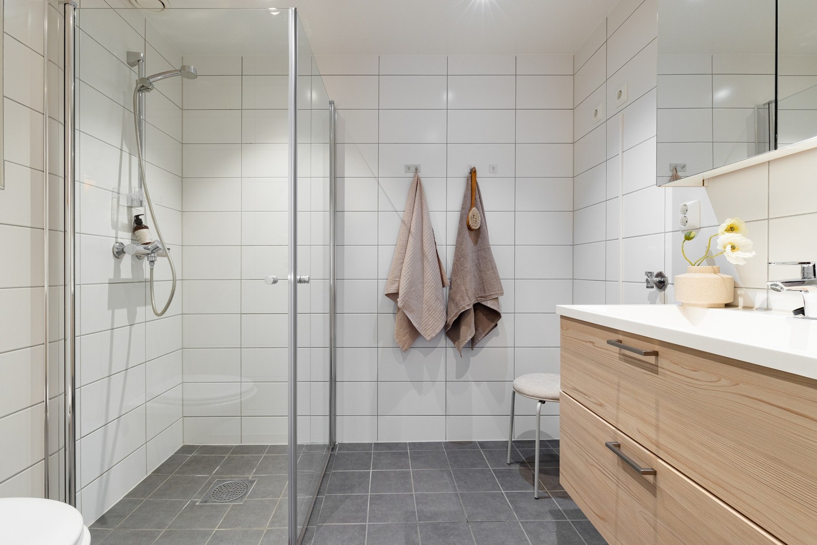 Badet er romslig og utstyrt med åpen dusj med dusjvegger i glass, vegghengt toalett, gulvvarme og downlights i tak. Galleribilde