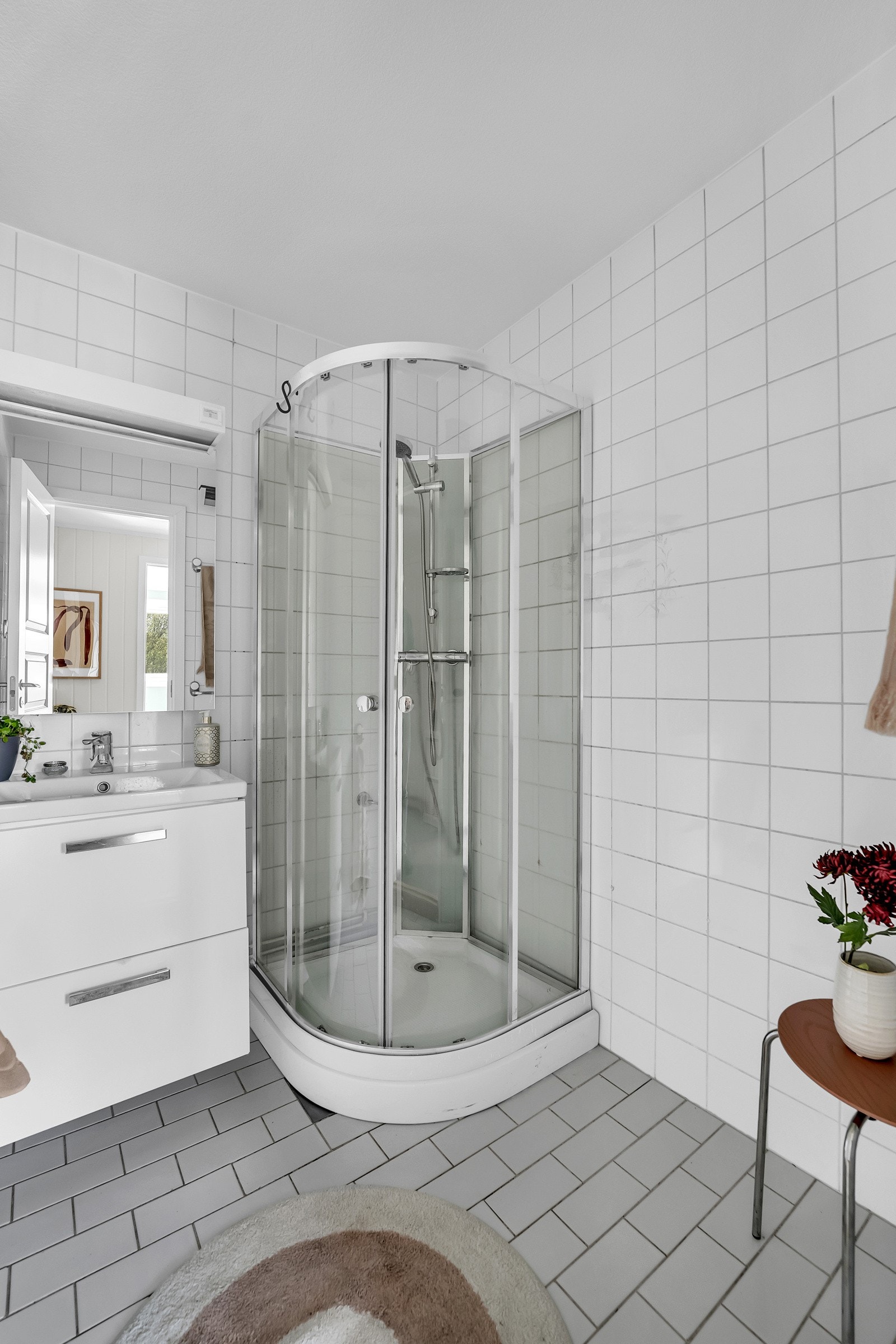 Boligen har et eldre bad, med hvite fliser på gulv og vegger, baderomsinnredning, speil, dusjkabinett og oppvarming med stråleovn. Galleribilde