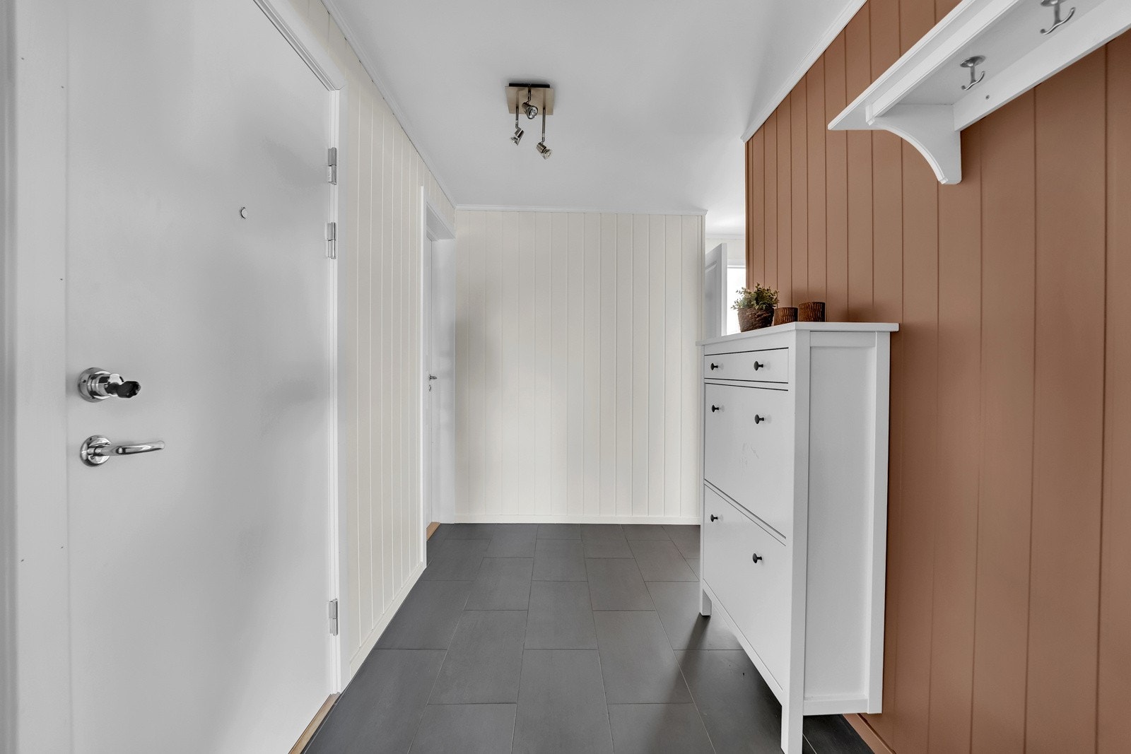 Entreen har mørke fliser på gulv, malte panelplater på veggene og glatt, hvitmalt himling. Galleribilde