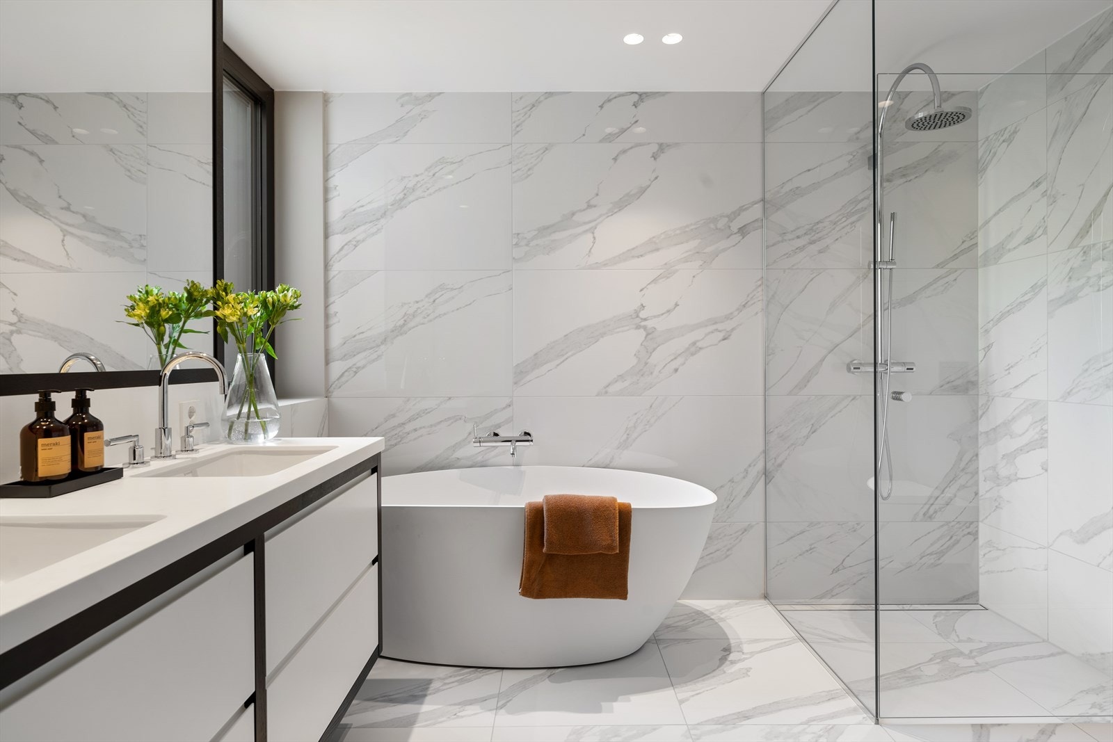 Baderomsinnredning bestående av benkeskap med glatte fronter - Hel benkeplate med to underlimte kummer og innfelt speil over servant - Designsluk i dusj og nedsenket felt i dusjen Galleribilde