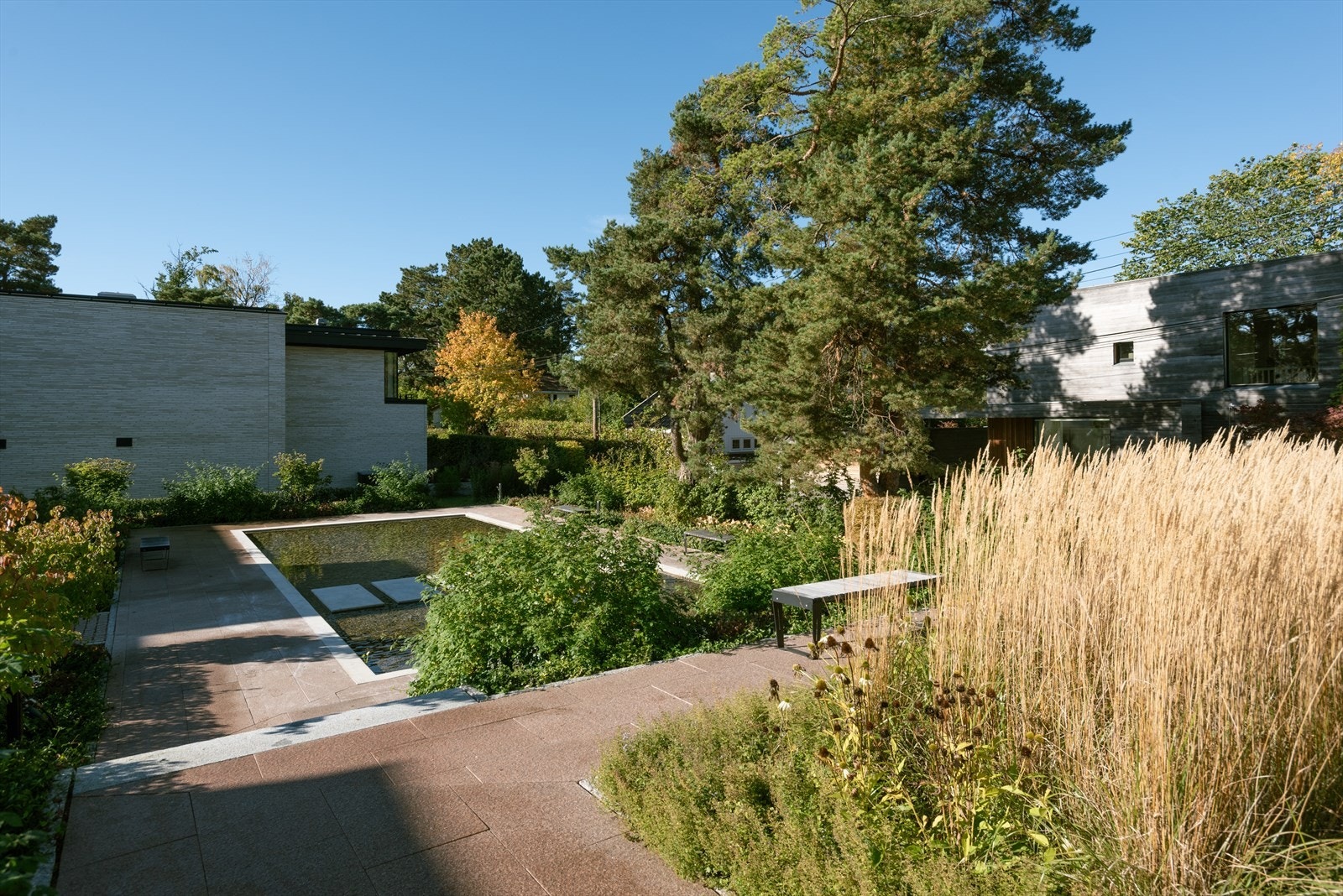 Vannspeilet reflekterer sollyset gjennom dagen, og de private hagene, som omkranser fellesområdet, skaper en følelse av en grønn oase midt i byen Galleribilde