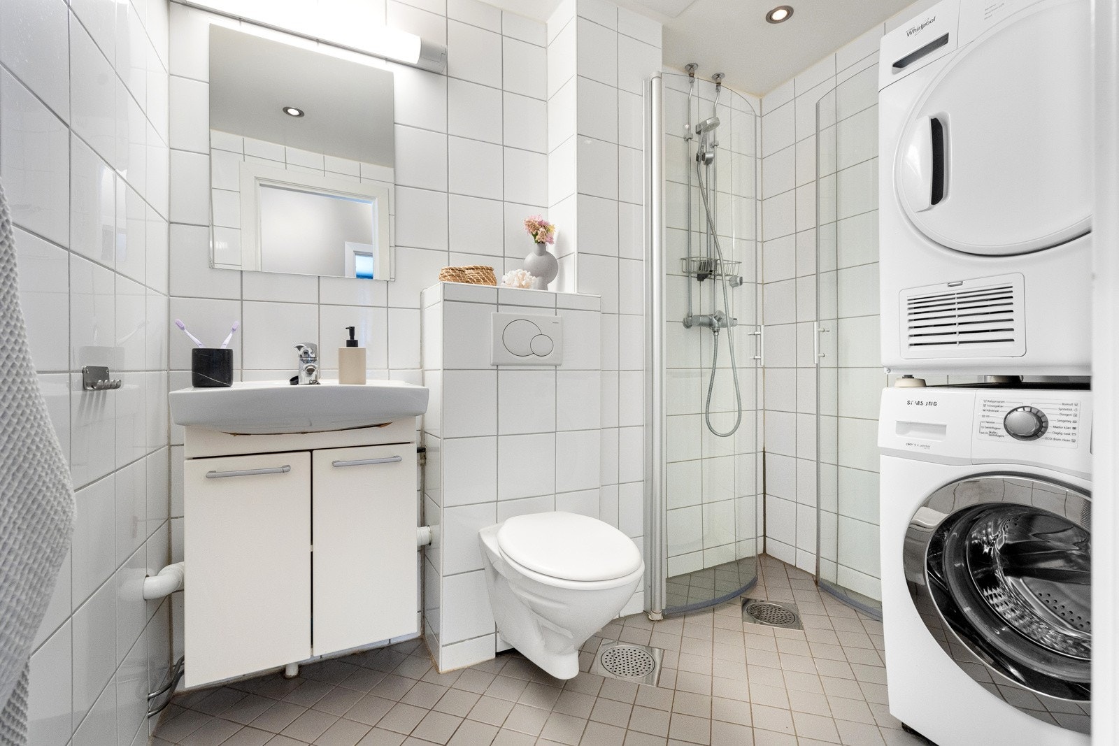 Pent, flislagt baderom som består av toalett, servant over innredning, speil og dusjhjørne. Galleribilde