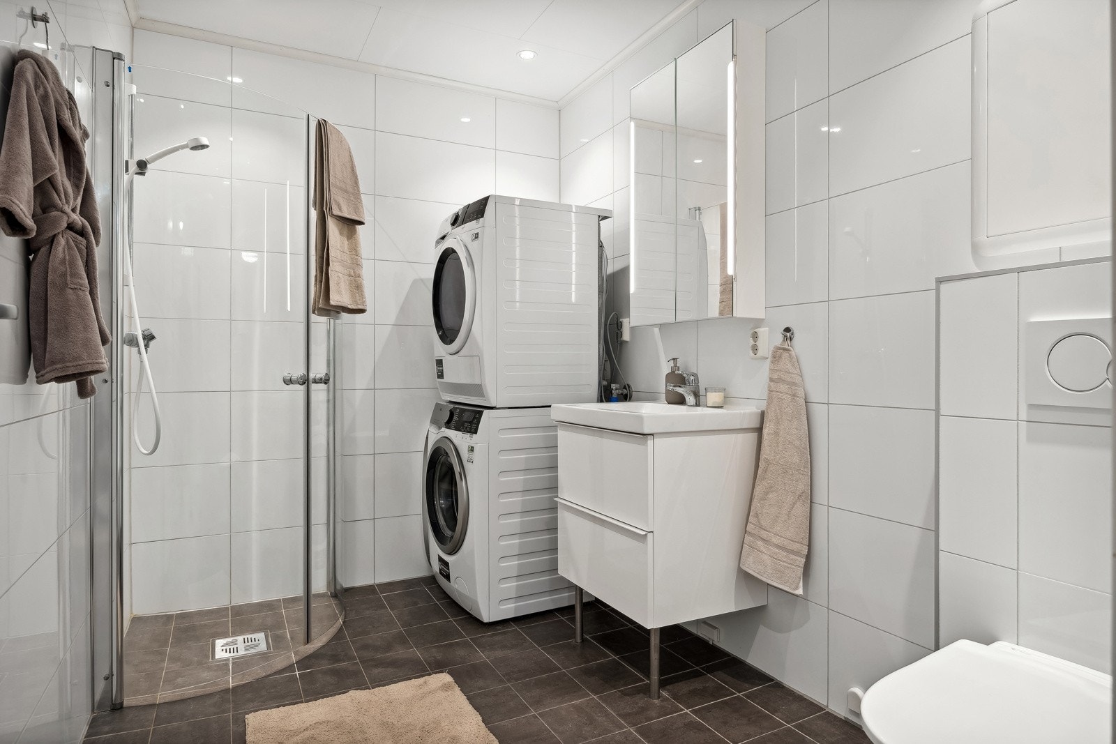 Pent baderom med moderne innredning, dusjhjørne og vegghengt toalett. Det er opplegg til vaskemaskin. Galleribilde