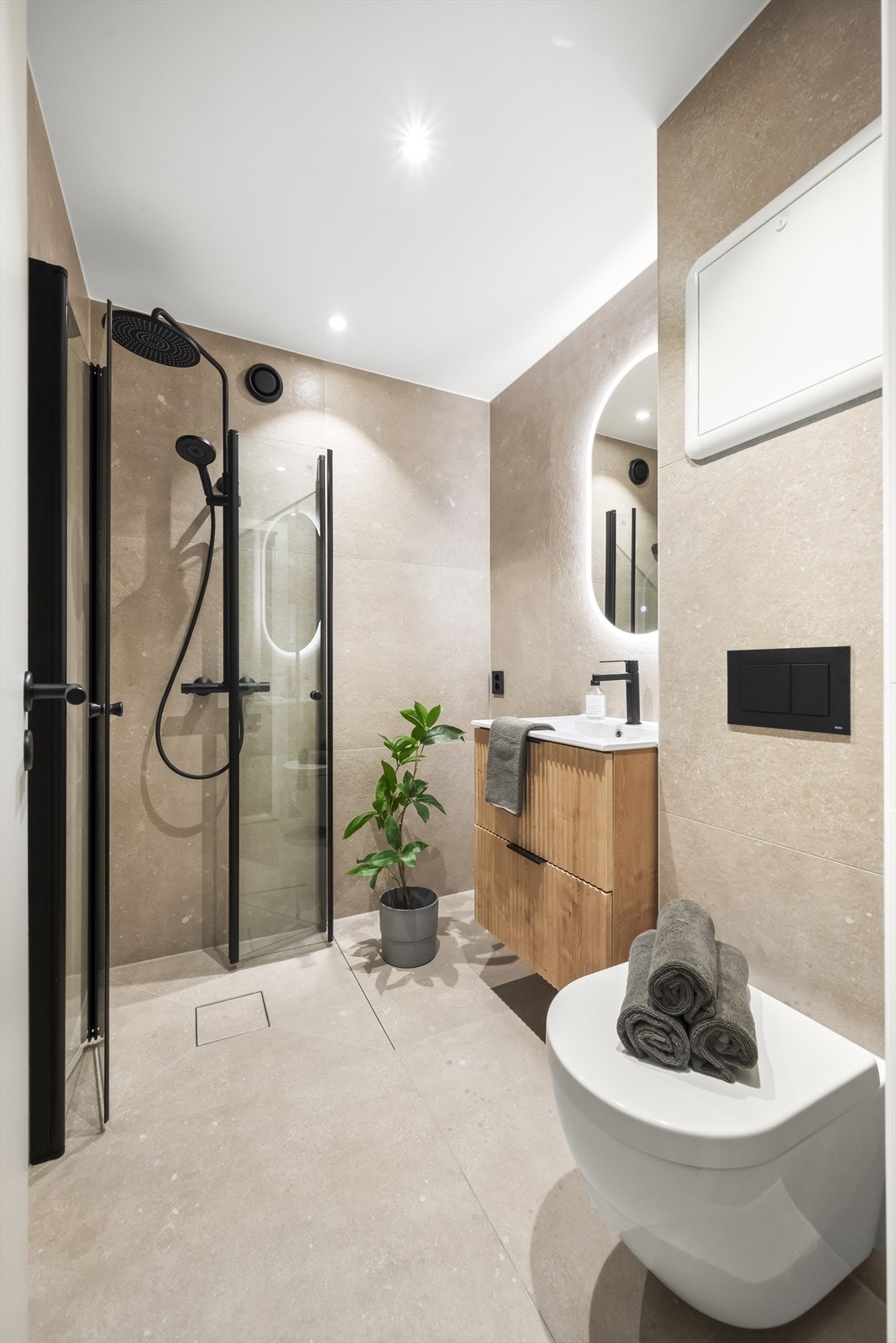 Rommet er innredet med vegghengt toalett, dusjhjørne med svingbare glassdører og baderomsinnredning med servant, skuffer og vegghengt speil med belysning. Galleribilde