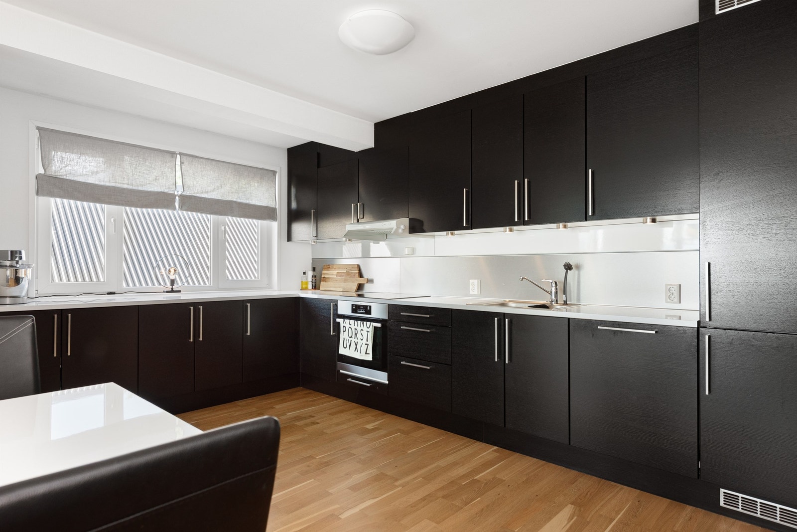 Sort kjøkkeninnredninbg fra HTH med laminat benkeplate og nedfelt oppvaskkum med ett-greps køkkenarmatur. Det er integrert stekeovn, platetopp med komfyrvakt, oppvaskmaskin og kjøleskap med fryser Galleribilde