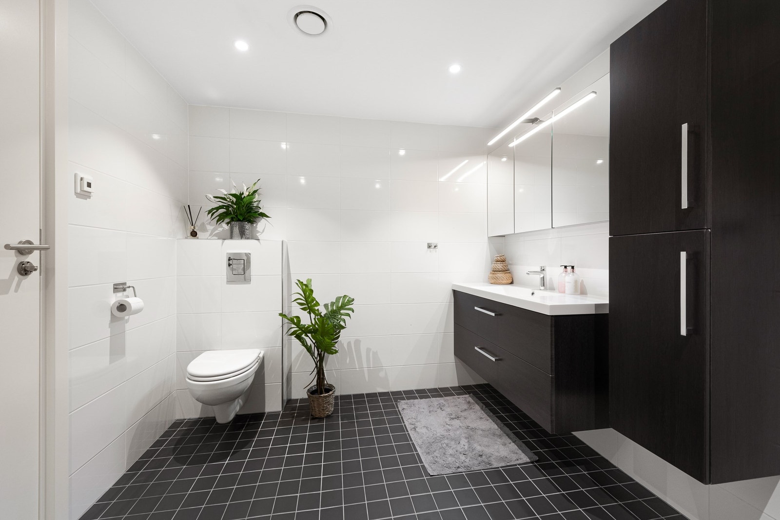 Romslig flislagt bad med gulvarme. Stor servantinnredning med skuffer, ovenpåliggende servant med ett-greps armatur. I tillegg vegghengt møbel. Dusjhjørne med dører og vegghengt armatur. Vegghengt toalett. Galleribilde