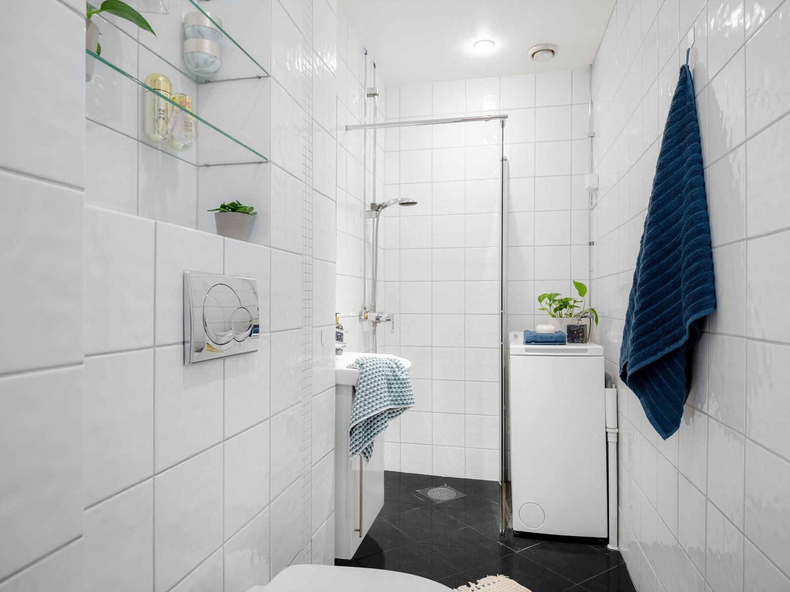 Lyst og tidløst baderom med hvite fliser på vegger samt opplegg og plass til vaskemaskin. Galleribilde