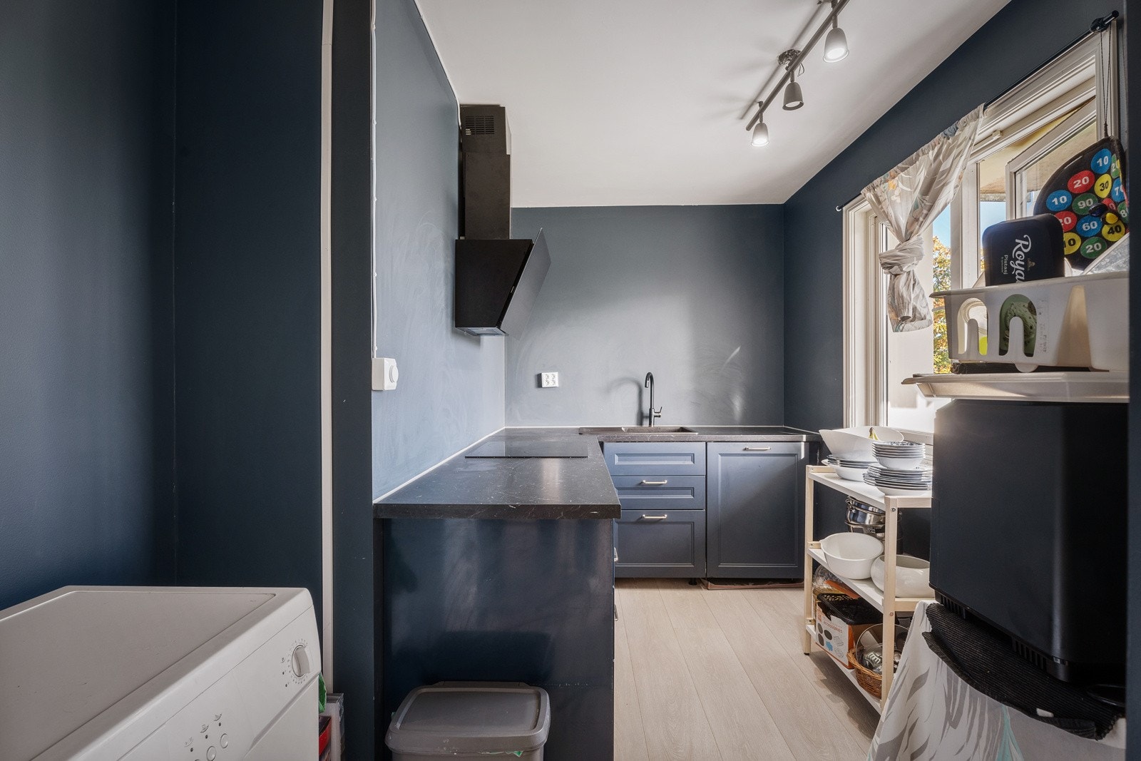 Kjøkkeninnredning med profilerte fronter. Laminat benkeplate med nedfelt kum i rustfritt stål. Ventilator med omluft. Opplegg for oppvaskmaskin og vaskemaskin. Induksjonstopp og stekeovn er integrert i innredningen. Galleribilde