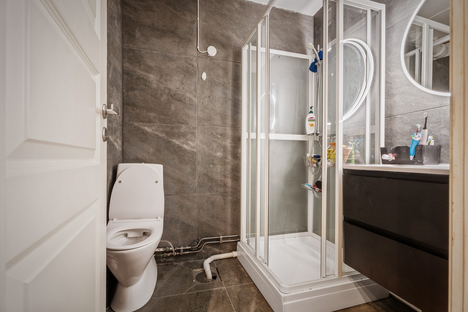 Flislagt bad med gulvvarme. Badet er utstyrt med servant med innredning, speil med innebygd belysning, dusjkapinett og frittstående toalett. Galleribilde
