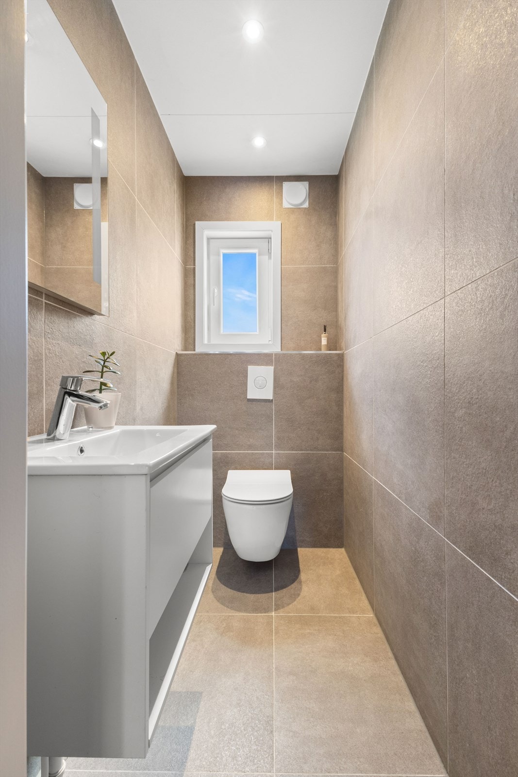 Toalettrommet ble renovert i 2022, og er med fliselagte overflater på vegger og gulv. Rommet er utstyrt med servantinnredning og vegghengt toalett. Et praktisk rom ved besøk! Galleribilde