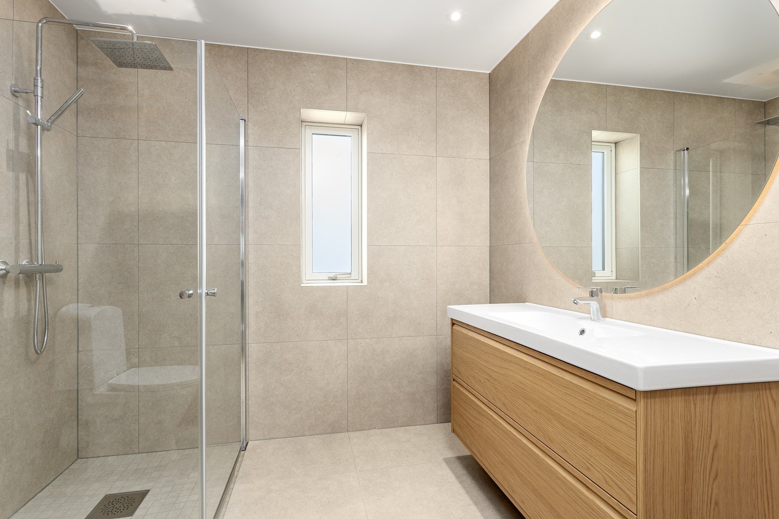 Tidløst bad innredet med heldekkende nedfelt servant med skuffeseksjoner, speil med LED lys, vegghengt toalett og dusjhjørne med regndusj og innfellbare dusjvegger. Galleribilde