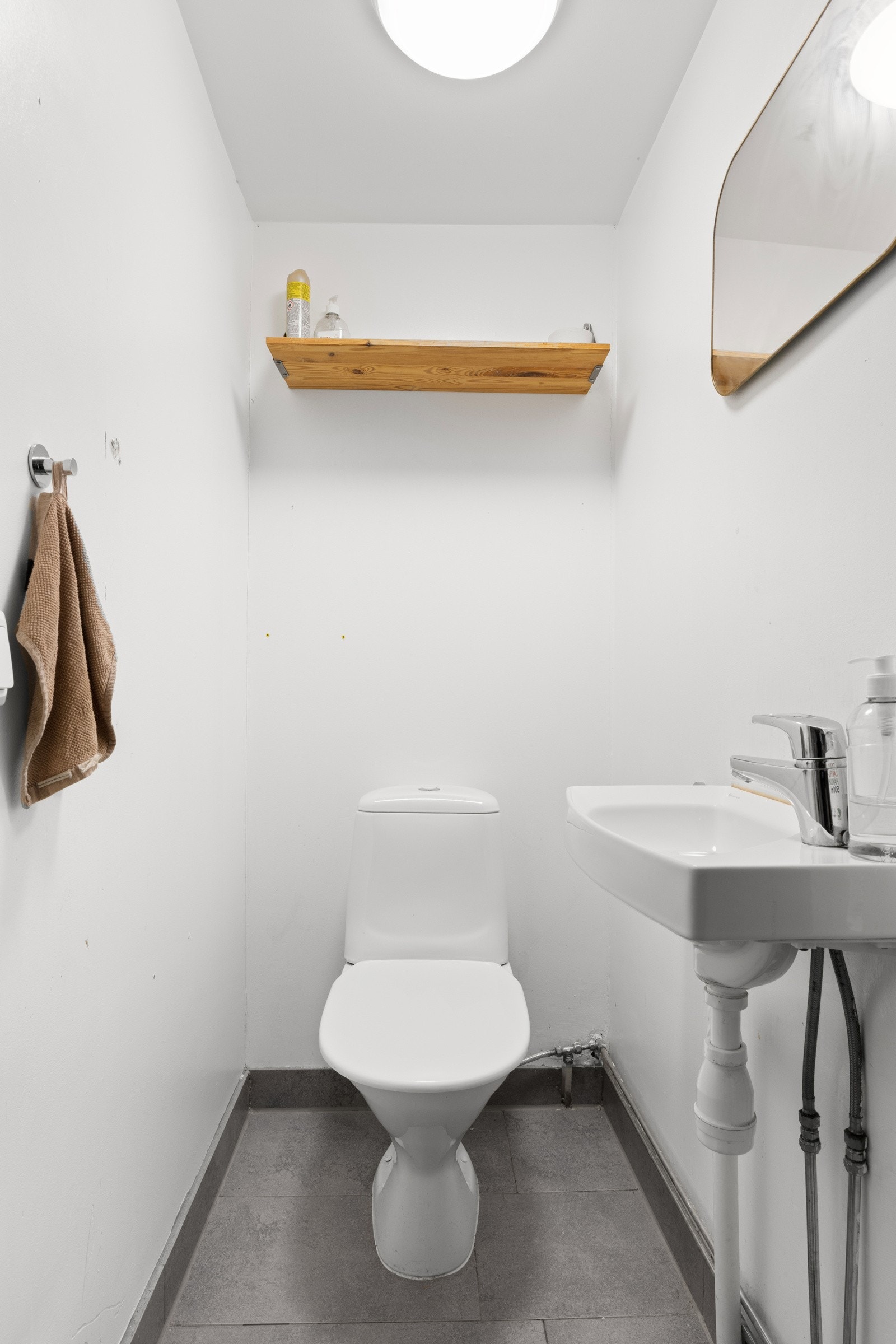 Enkelt toalettrom med frittstående toalett og servant m/ bl.batteri. Det er lagt fliser på gulv og malte overflater. Galleribilde