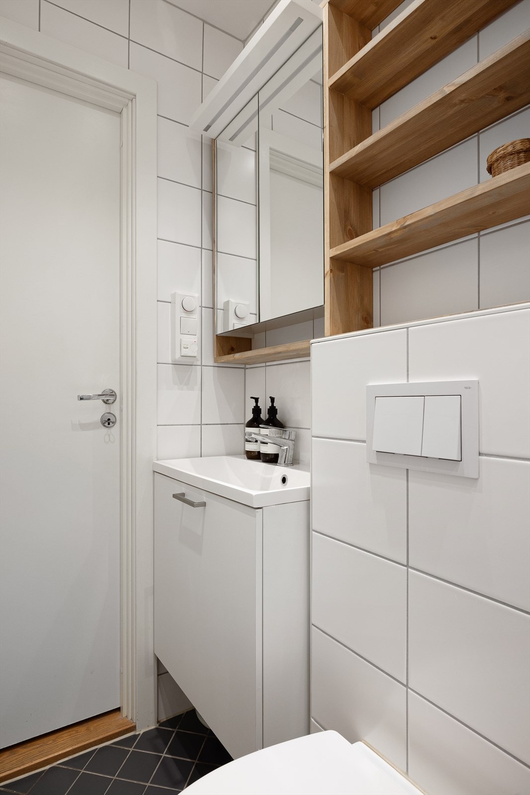 Badet er utstyrt med dusjhjørne med innfellbare dusjdører, veggmontert toalett og baderomsinnredning med servant, blandebatteri, skuffer og vegghengt speilskap Galleribilde