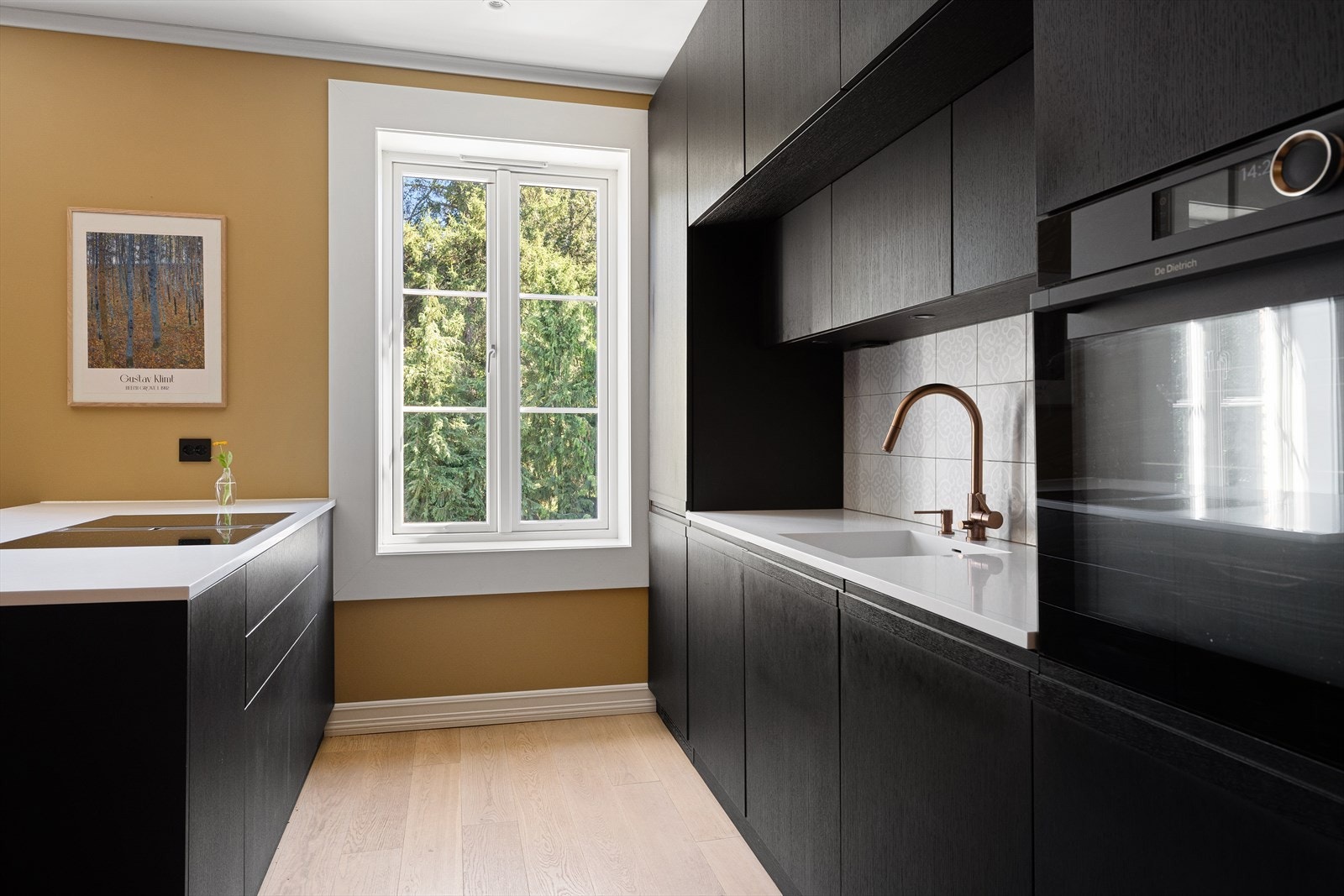 Møbelsnekret/plassbygd kjøkken med et tidsriktig uttrykk. Innredning med mørke, glatte fronter, fliser på veggen over kjøkkenbenk og Corian benkeplate Galleribilde