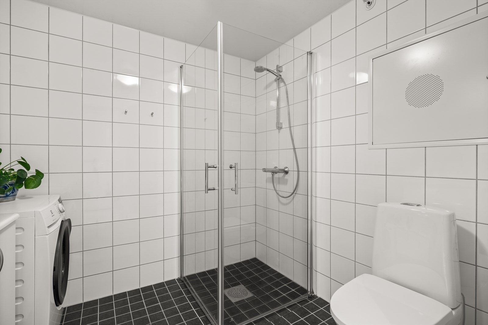 Innredning og garnityr på bad fremstår med veggmonterte dusjdører, servant med underskap, speilskap med lys, opplegg for vaskemaskin og veggmontert wc. Galleribilde