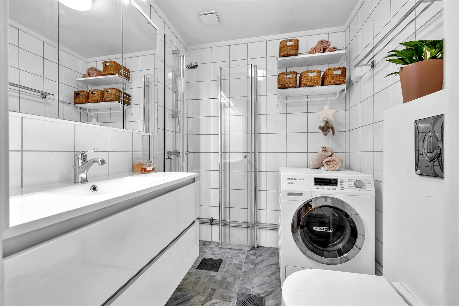 Pent flislagt bad med stor servant med skap og tilhørende speilskap. Dusjhjørne, toalett og opplegg for vaskemaskin. Galleribilde