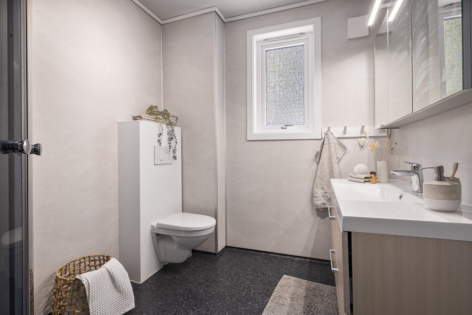 Badet er lyst og flott og inneholder vegghengt toalett, helstøpt servant, skuffer under servant med slette fronter, dusjkabinett og opplegg for vaskemaskin. Galleribilde