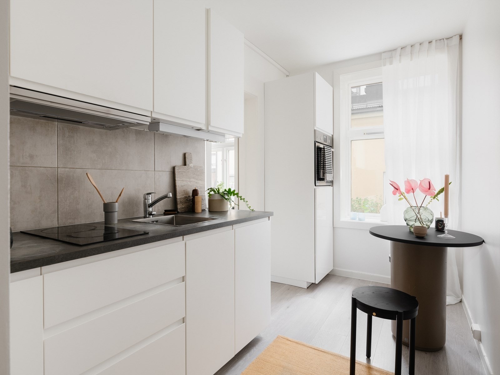 Tidløst kjøkken med en lekker kombinasjon av lyse, slette overflater, integrert grep og sort benkeplate. Galleribilde