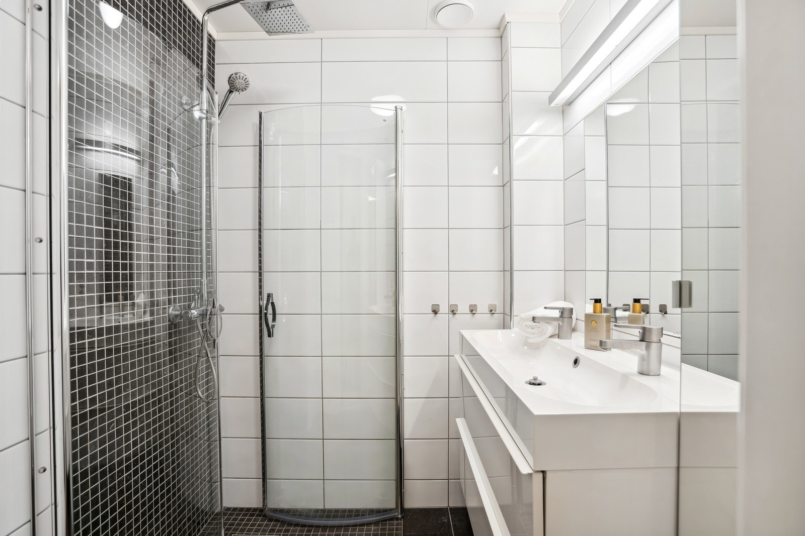 Moderne og stilig bad som inneholder dusjhjørne med waterfall-dusjhode, servant, speil og god belysning Galleribilde