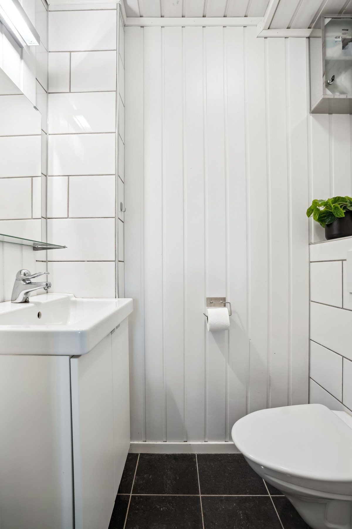 Praktisk toalettrom med fliser på gulv og delvis på vegger, god belysning, toalett og servant Galleribilde