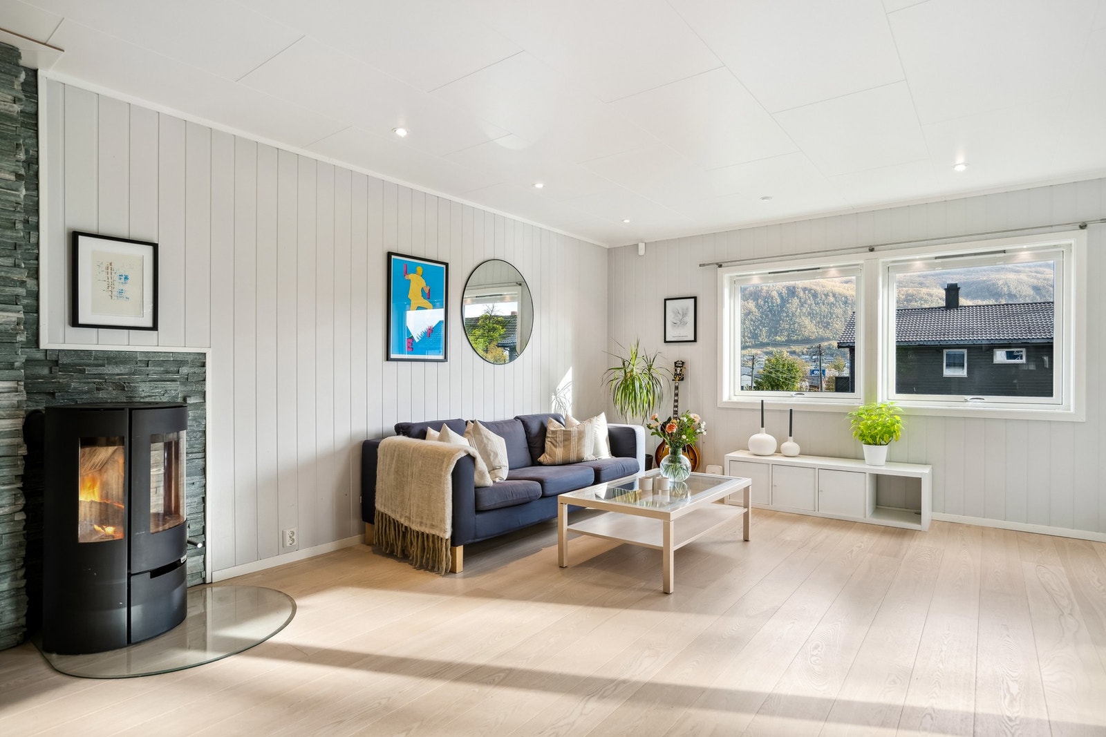 Boligen har en romslig og lys stue med vedovn som skaper en varm og hyggelig atmosfære Galleribilde