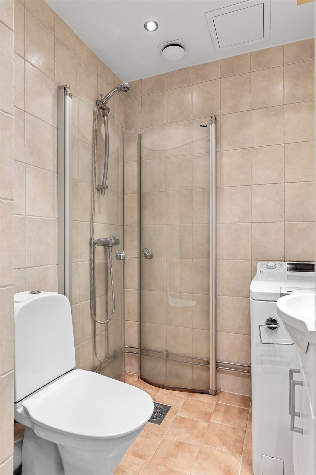 Badet inneholder toalett, innredning med servant, speilskap med belysning og dusjhjørnet rett på gulv med innfellbare glassdører. Galleribilde