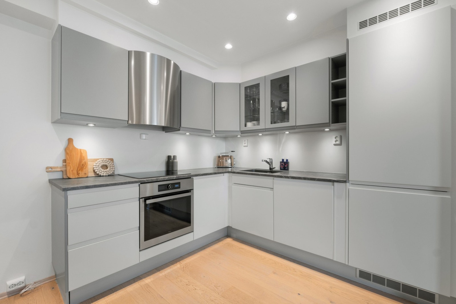 Innredet med glatte fronter, laminat benkeplate, nedfelt komfyrtopp, underlimt vask og lys under overskap. Galleribilde