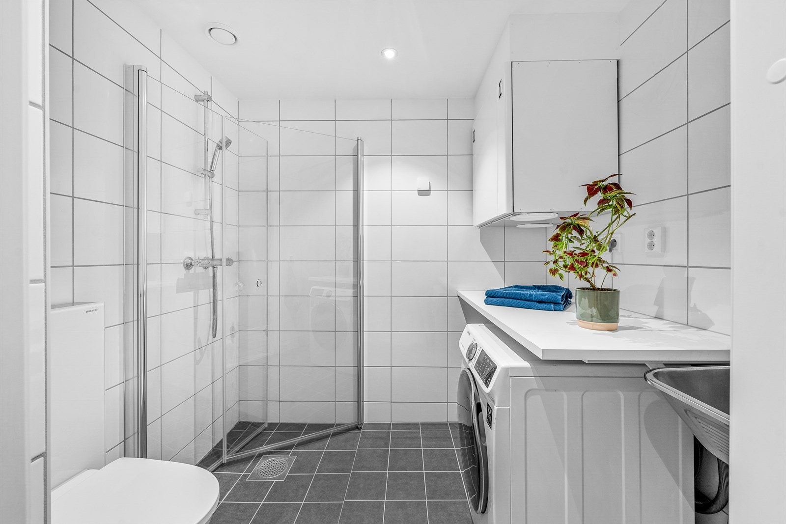 Det andre badet har nedsenket dusjhjørne med rette, innfellbare glassdører og en god arbeidsbenk. Under benken er det opplegg for vaskemaskin og ved siden av er det skyllekum i stål. Galleribilde