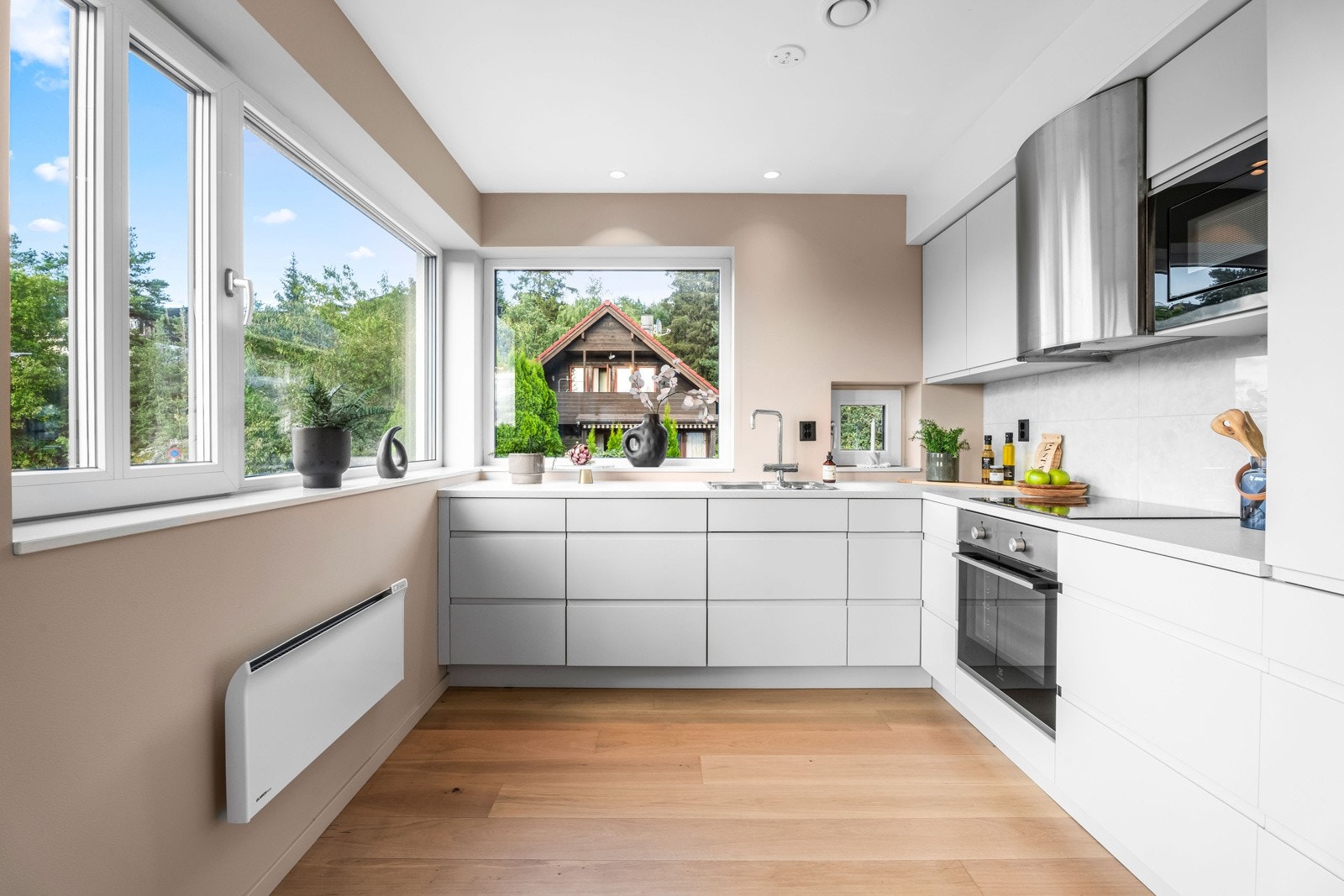 Glatte lysegrå fronter med lys laminatbenkeplate med nedfelt kum i rustfritt stål og marmor flisfelt på vegg. Galleribilde