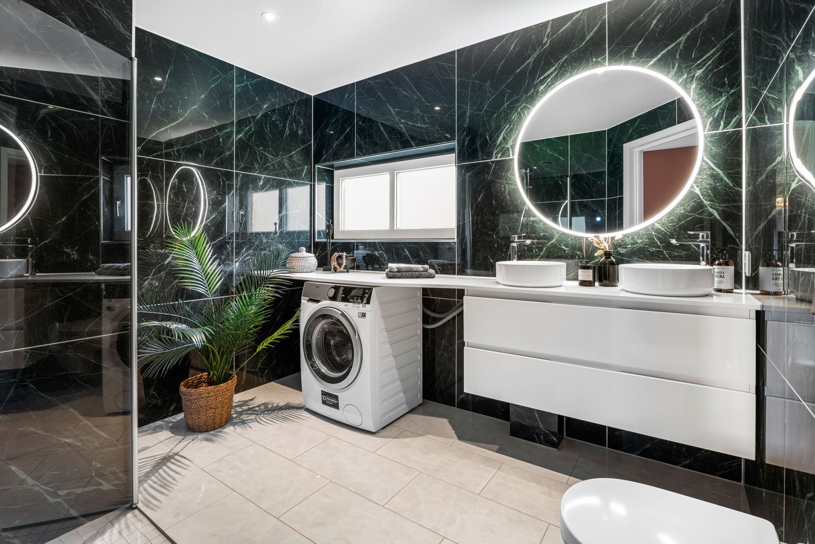 Lukrativt bad med 90x90 grønne marmorfliser og vegg til-vegg benkeplate i hvit marmor, dobbel servant og innredning. Galleribilde