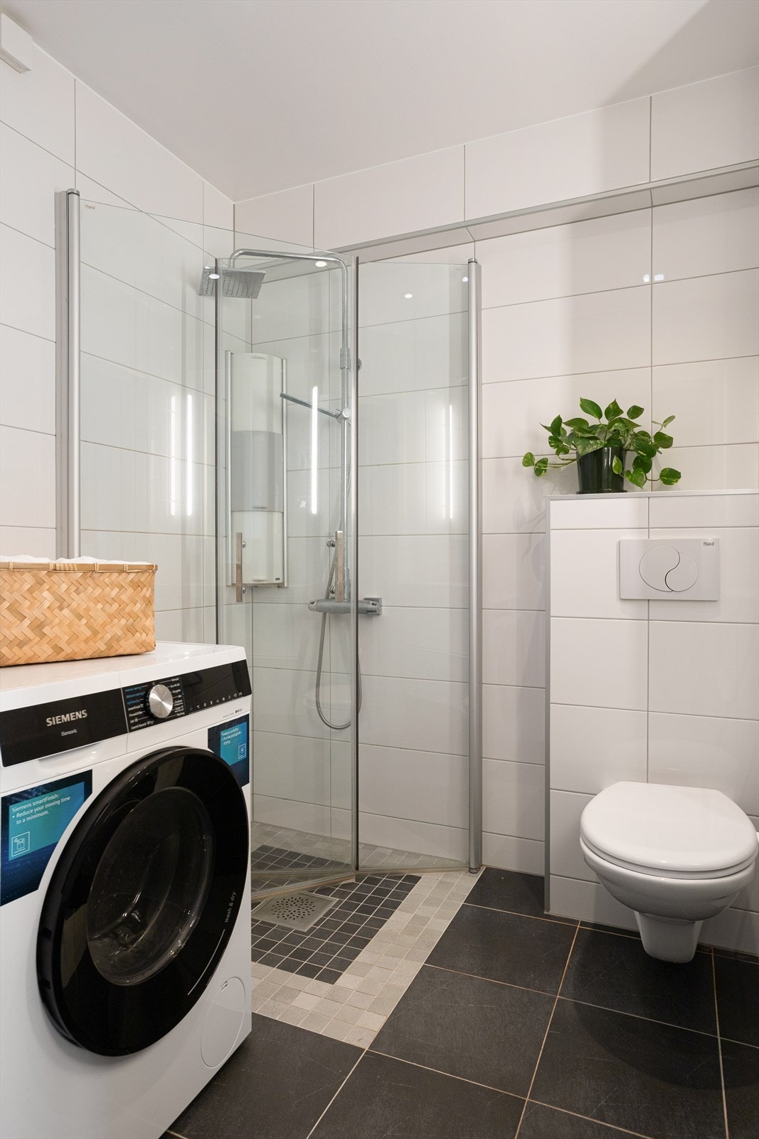 Badet er utrustet med veggmontert innredning med heldekkende servant, dusjnisje med glassdører, vegghengt toalett, samt opplegg for vaskemaskin og tørketrommel. Galleribilde