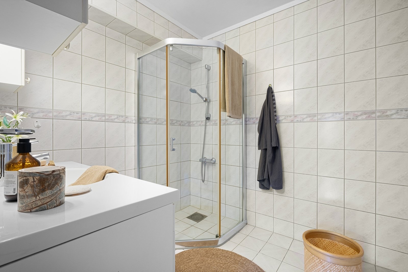 Badet har fliser på gulv og vegger og inneholder dusjhørne og servantmøbler. Galleribilde