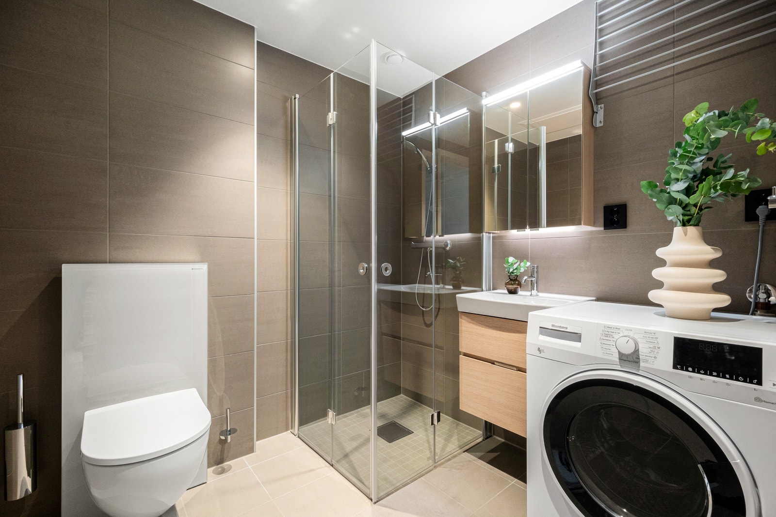 Moderne flislagt bad med veggehengt wc, varmekabler og dusj. VASKEMASKIN KOMBINERT TØRKETROMMEL Galleribilde