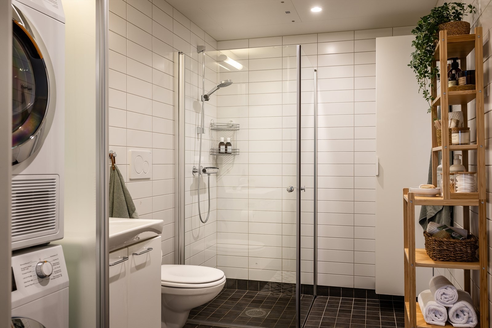 Videre er badet innredet med vegghengt klosett, servant på innredning og dusjhjørne med svingbare dører. Galleribilde