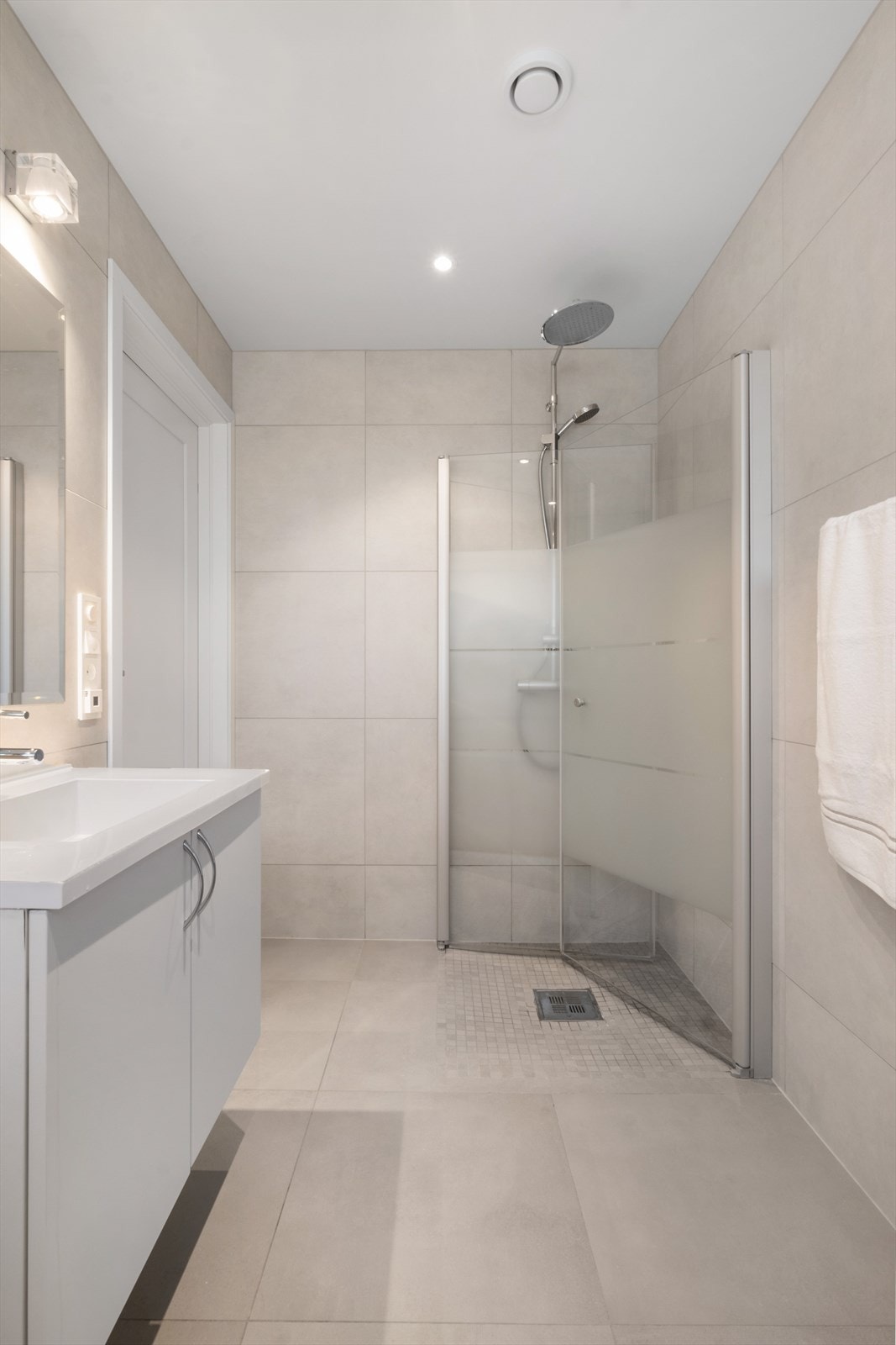 Boligen har 2 bad i hoveddelen. Her fra badet i første etasje. Store fliser på gulv og vegger. LItt mindre i selve dusjsonen. Dusj fra Oras med hånd og takdusj. Praktisk med innfellbare dusjvegger. Galleribilde