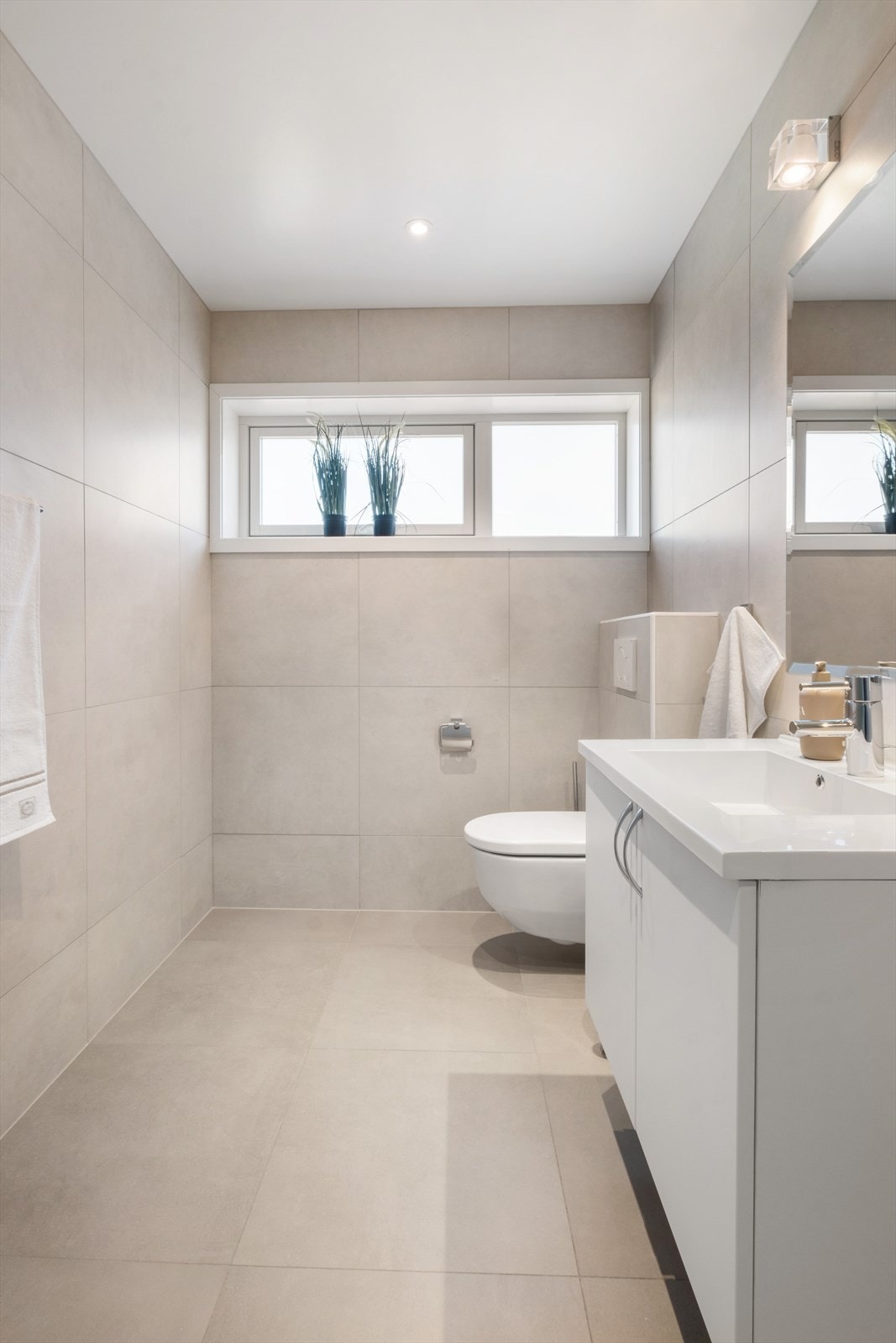 Lys innredning med skap, speil, pen belysning og downlights i tak. Videre er det vegghengt toalett og vinduer med "frosting" for å hindre innsyn Galleribilde