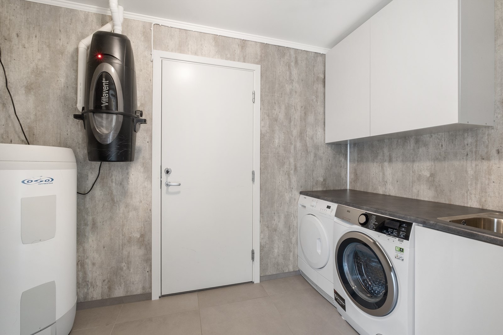 Meget praktisk vaskerom med varme i gulv. Innredning består av skap, benk og vask. Gjennomgang fra vaskerommet til garasjen. Galleribilde