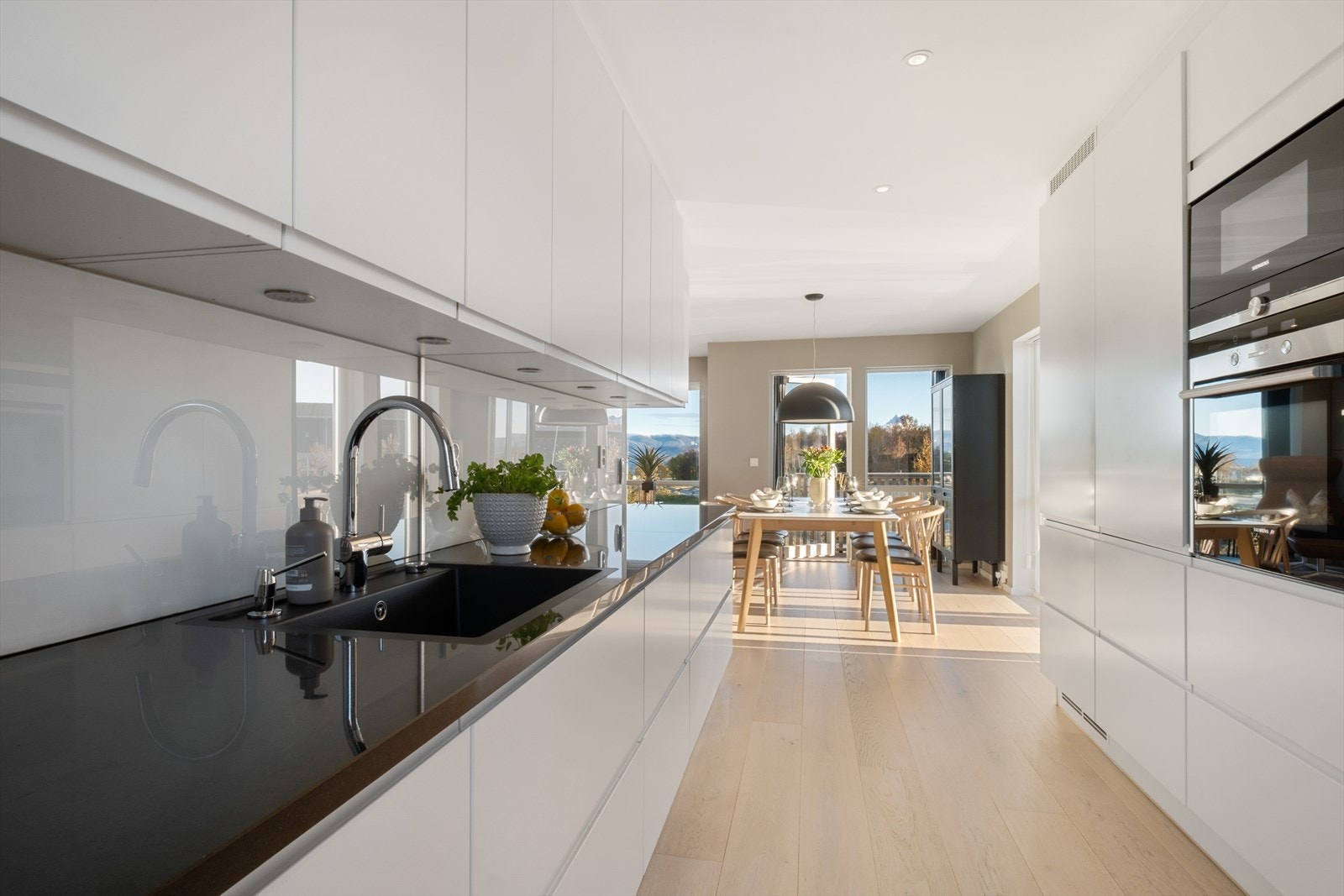 Lekkert kjøkken med glatte flater. Integrerte hvitevarer. Benkplater av stein med nedfelt sort vask. Spottbelysning også under overskap Galleribilde