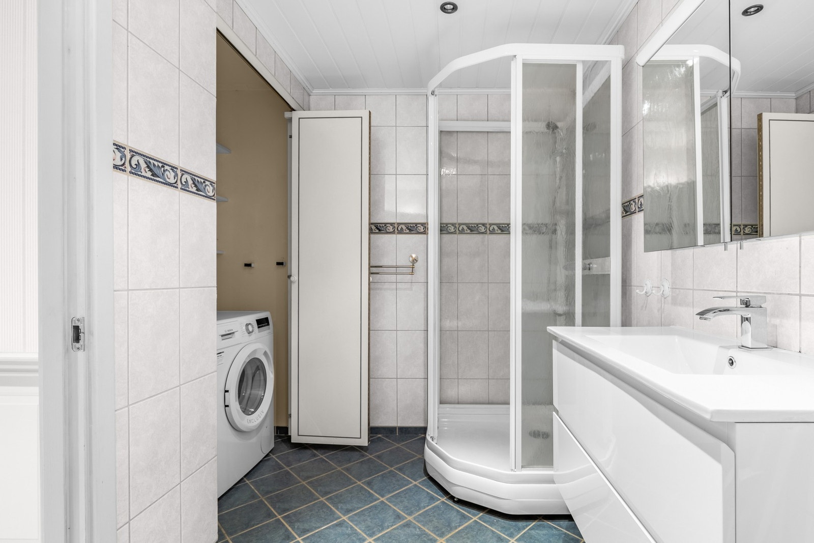 Badet har tidløse, nøytrale fliser på gulv og vegg samt gulvvarme. Dusjkabinett som får vannet til å renne kontrollkert ned i sluket. Galleribilde