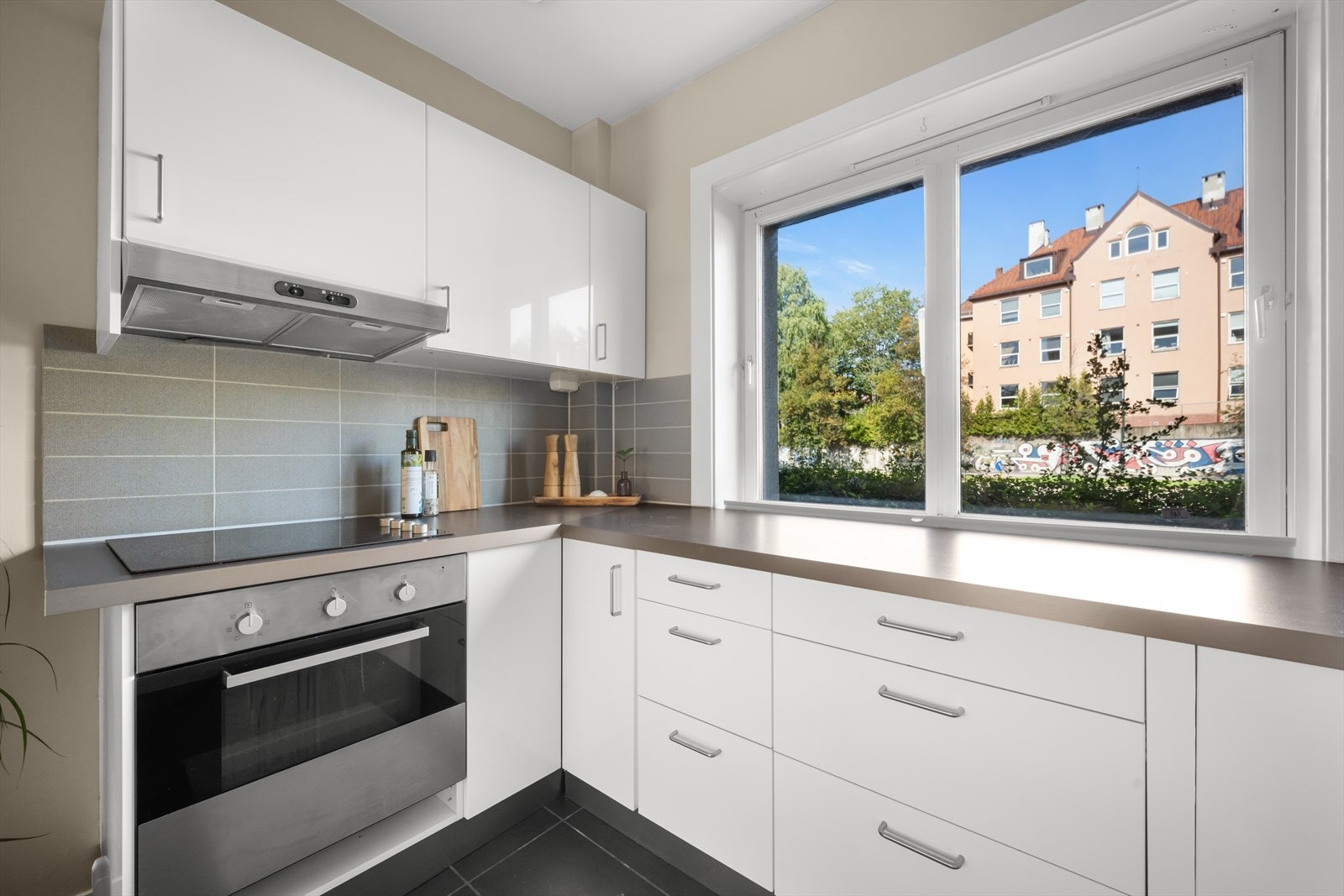 Hyggelig, separat kjøkkenrom med god arbeidsflate ved vinduet. Kjøkkeninnredningen er stilren med hvite, glatte fronter, fliser på bakvegg og laminert benkeplate. Galleribilde