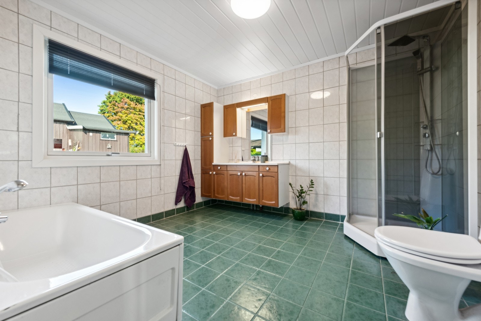 Romslig baderomsinnredning med både badekar og dusj. Stort og flott vindu som slipper inn rikelig med naturlig lys. Galleribilde