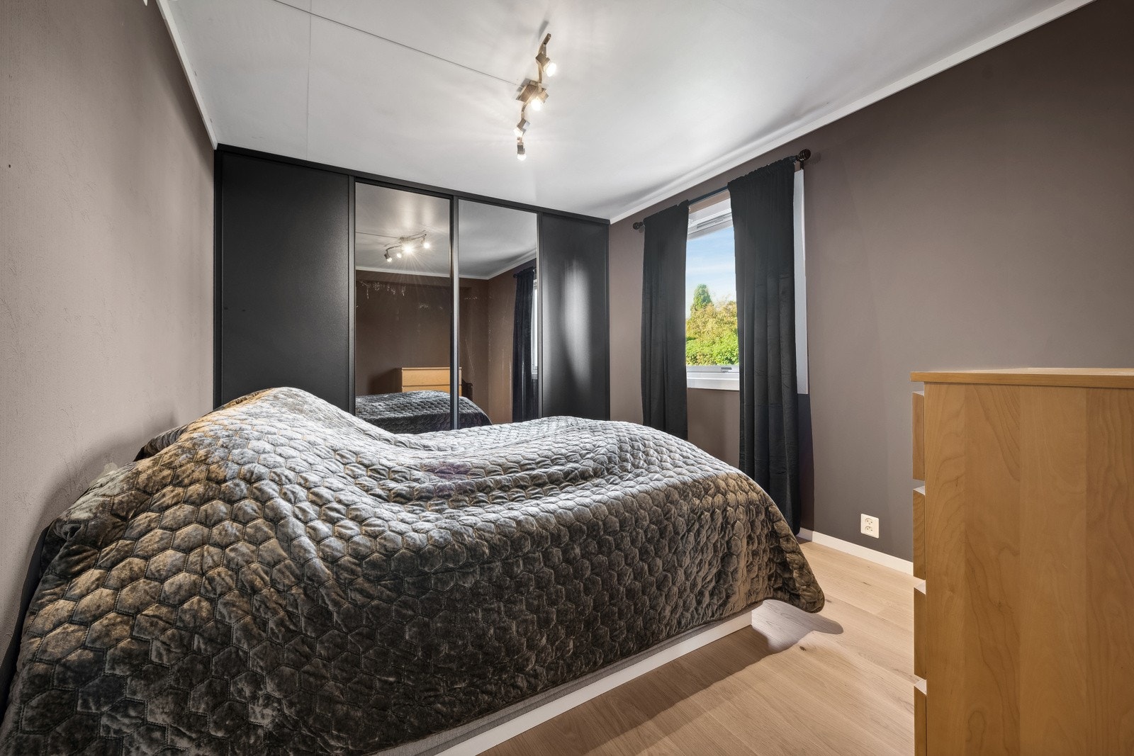 Moderne soverom med mørke vegger, speilfrontet garderobe og stort vindu som gir godt lysinnslipp. Galleribilde