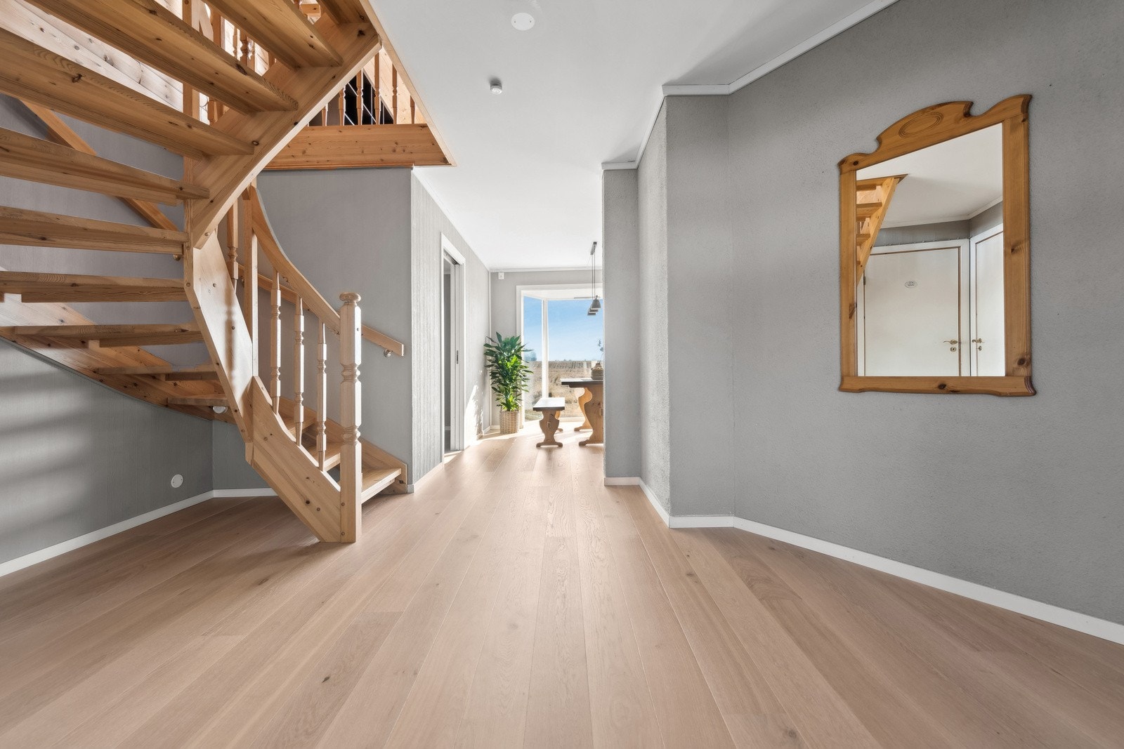 Romslig gang med lyse parkettgulv, åpen trapp i tre og god naturlig belysning. Galleribilde