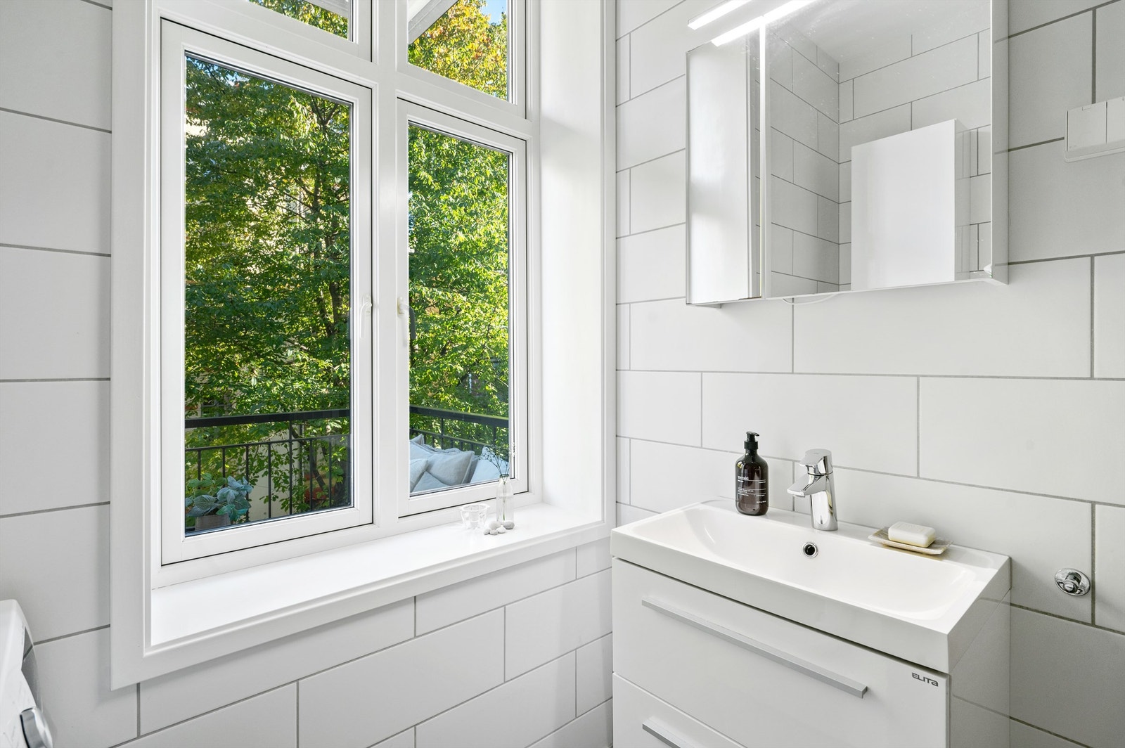 Badet er flislagt i tidløse farger med grå og hvite fliser på henholdsvis gulv og vegger, samt innredet med møbler som har oppbevaringsplass i både servant og speilskap. Galleribilde