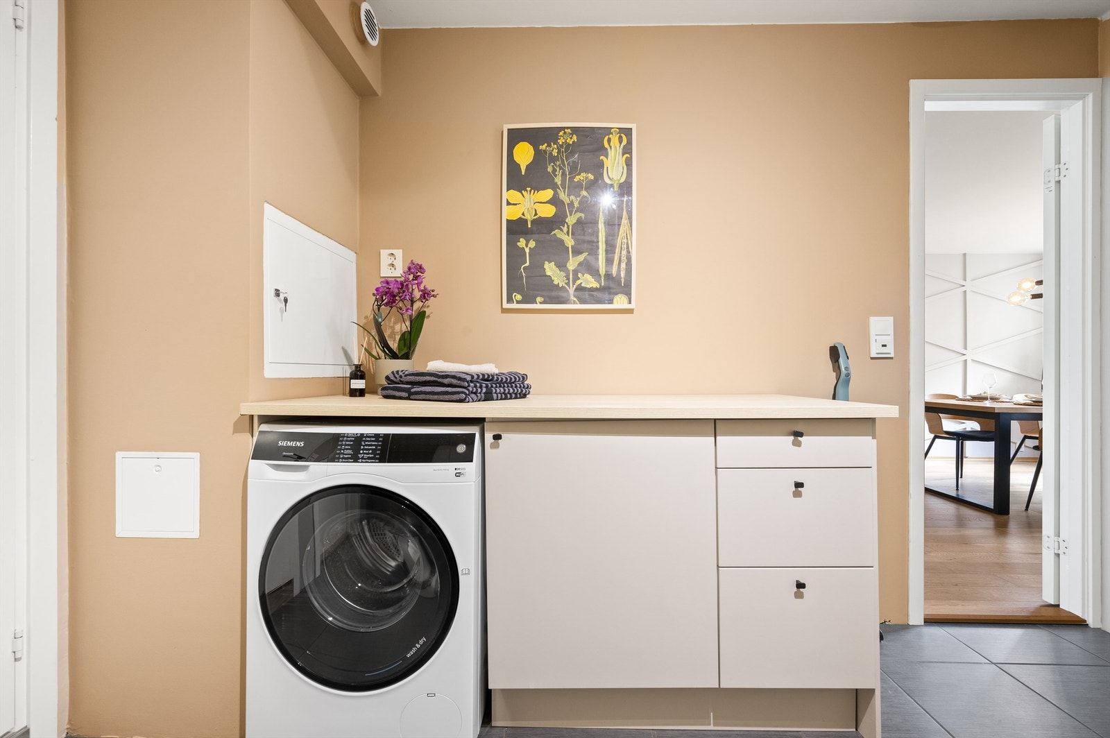 Videre har boligen også et eget vaskerom. Rommet har flislagt gulv med varme og vegghengte skap med glatte fronter. Det er opplegg for vaskemaskin. Galleribilde