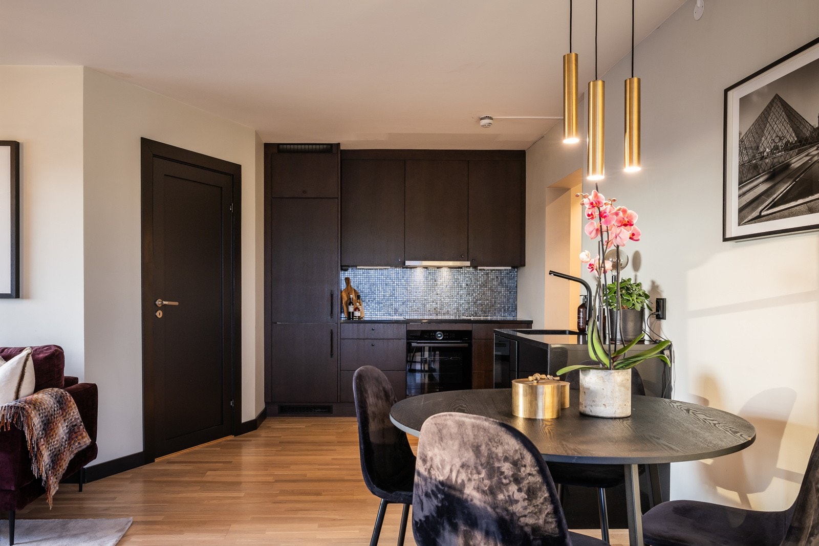 Moderne kjøkken i åpen løsning med tidsriktig glatt innredning ned soft close, granitt benkeplate med underlimt stålkum, fliser over benk og belysning under overskap. Galleribilde