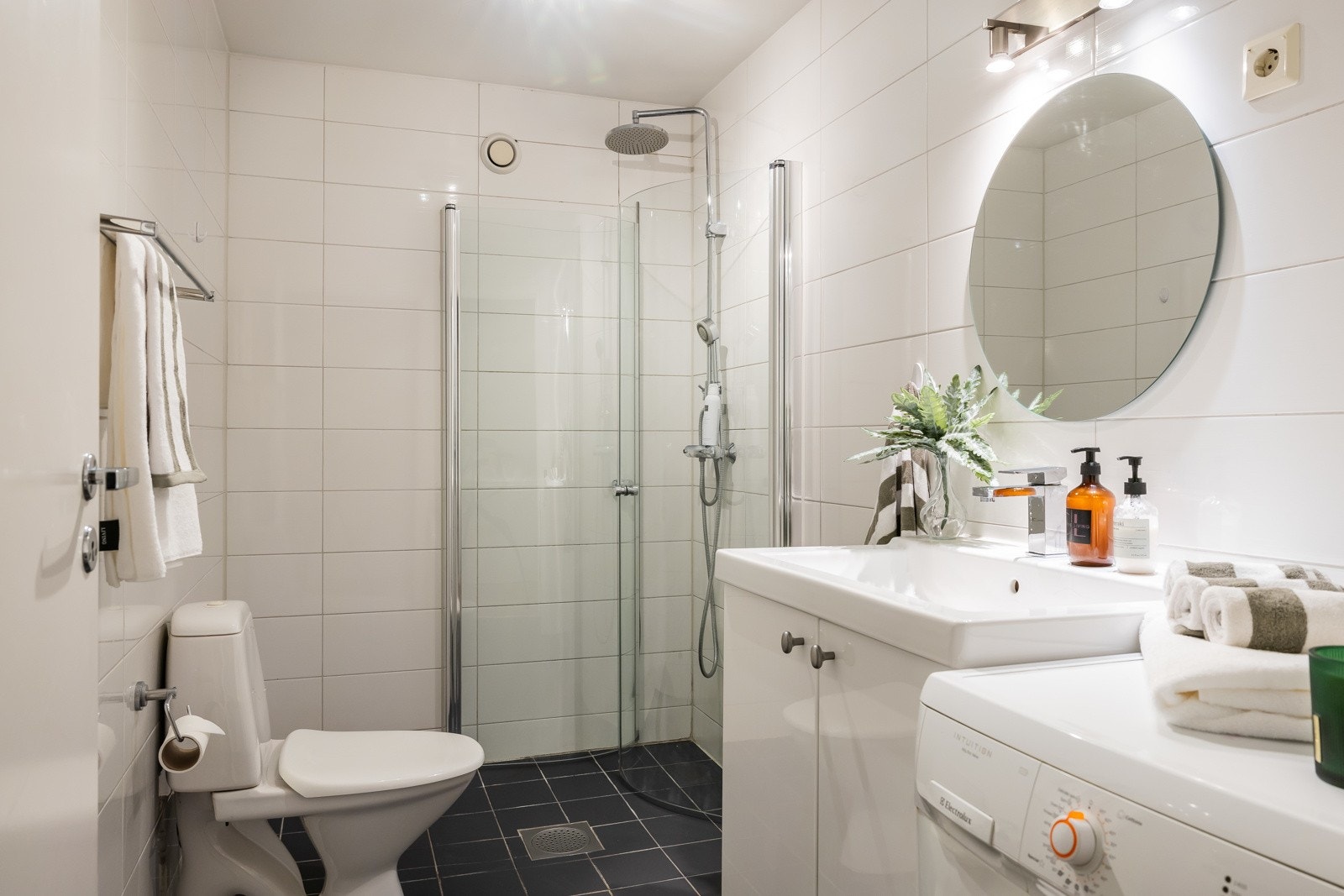 Leiligheten har romslig baderom med innredning bestående av servant med underskap, speil, gulvmontert klosett, dusjhjørne med svingbare glassdører og opplegg for vaskemaskin. Galleribilde